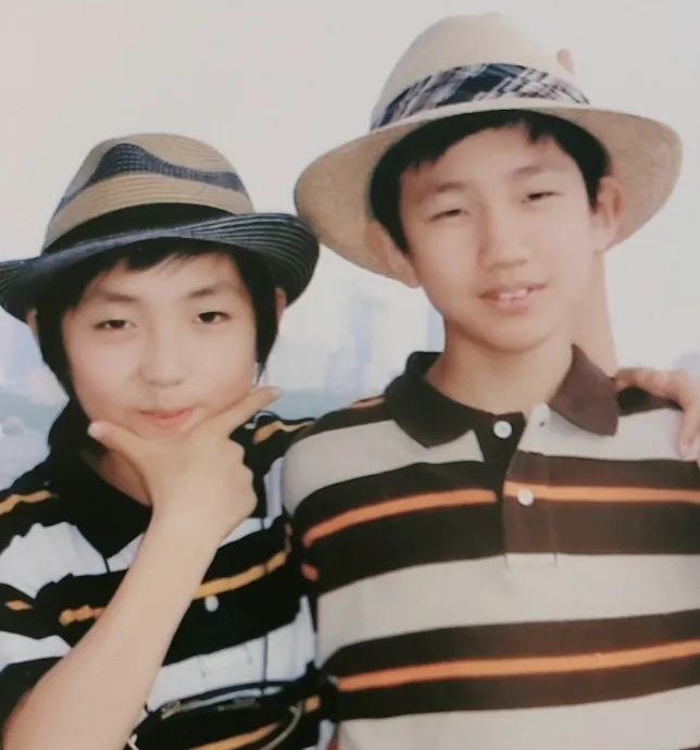 A childhood photo of two young boys in straw hats posing together, a city skyline behind them