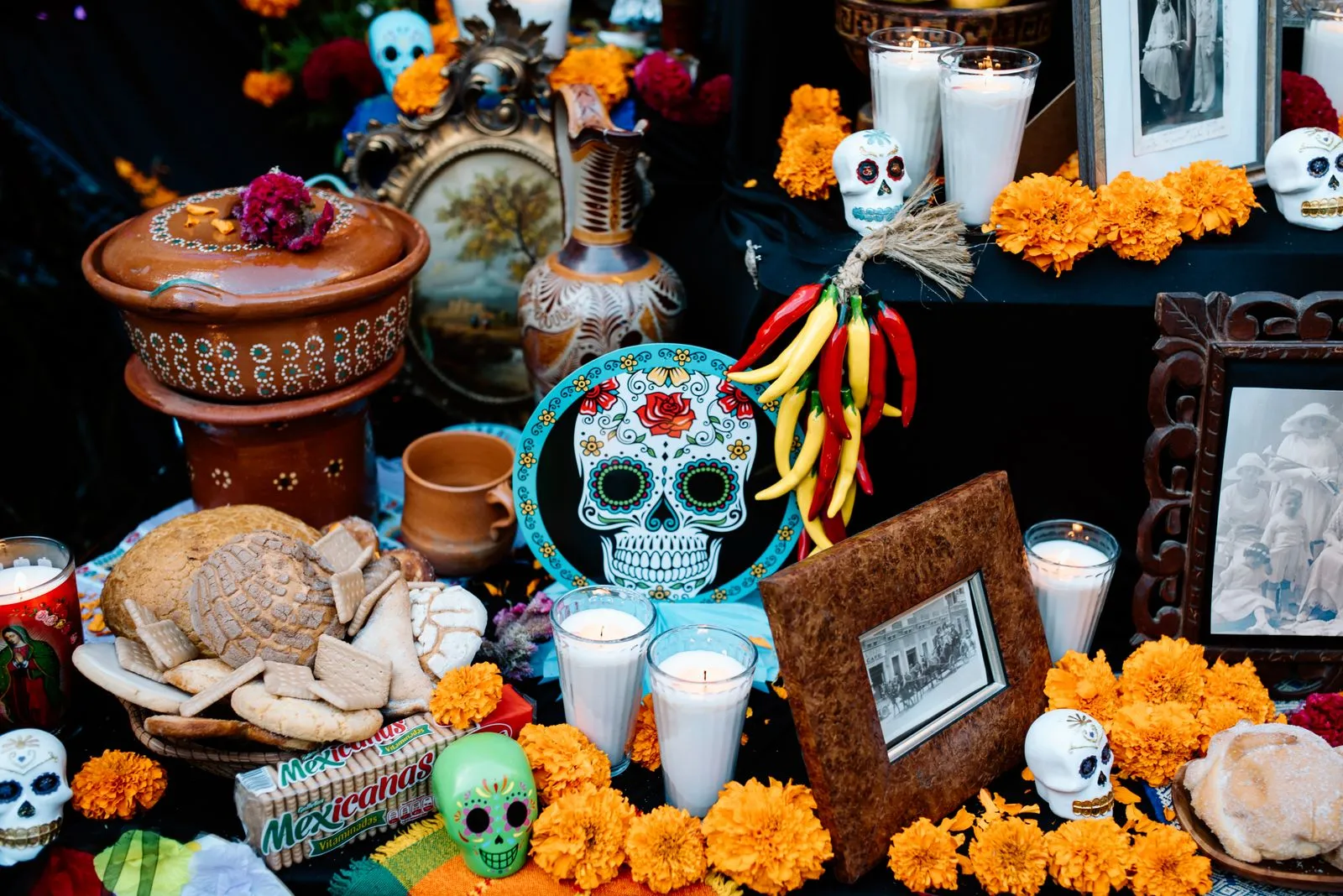 A traditional Día de los Muertos ofrenda laid with marigolds, lit candles, pan de muerto, sugar skulls, and framed family photographs