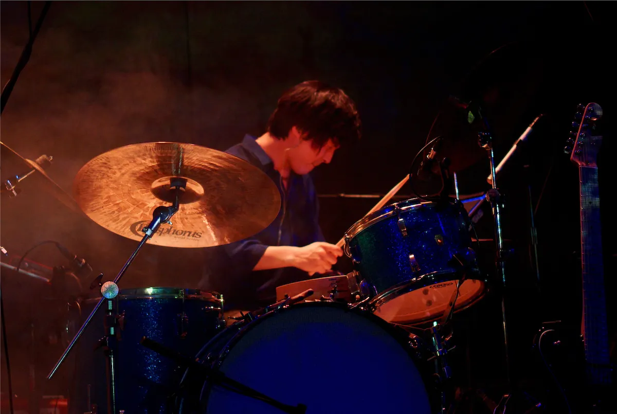 A drummer mid-performance behind a blue kit, lit by blue stage lights at a live show