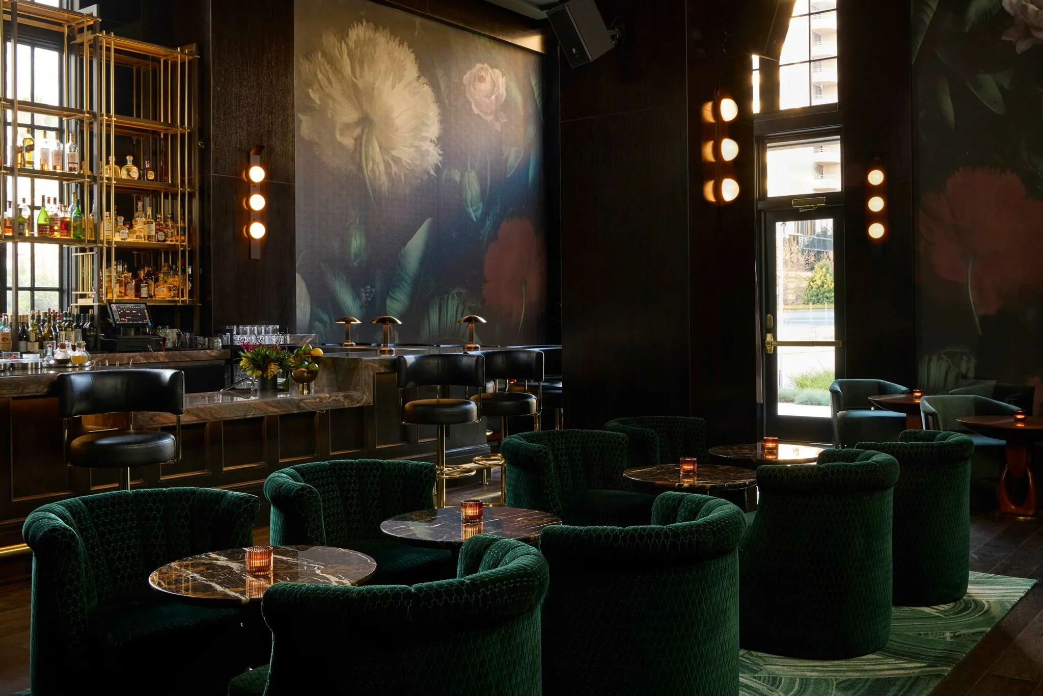 A moody speakeasy-style lounge at the Fairmont Breakers with green velvet armchairs and a floral mural