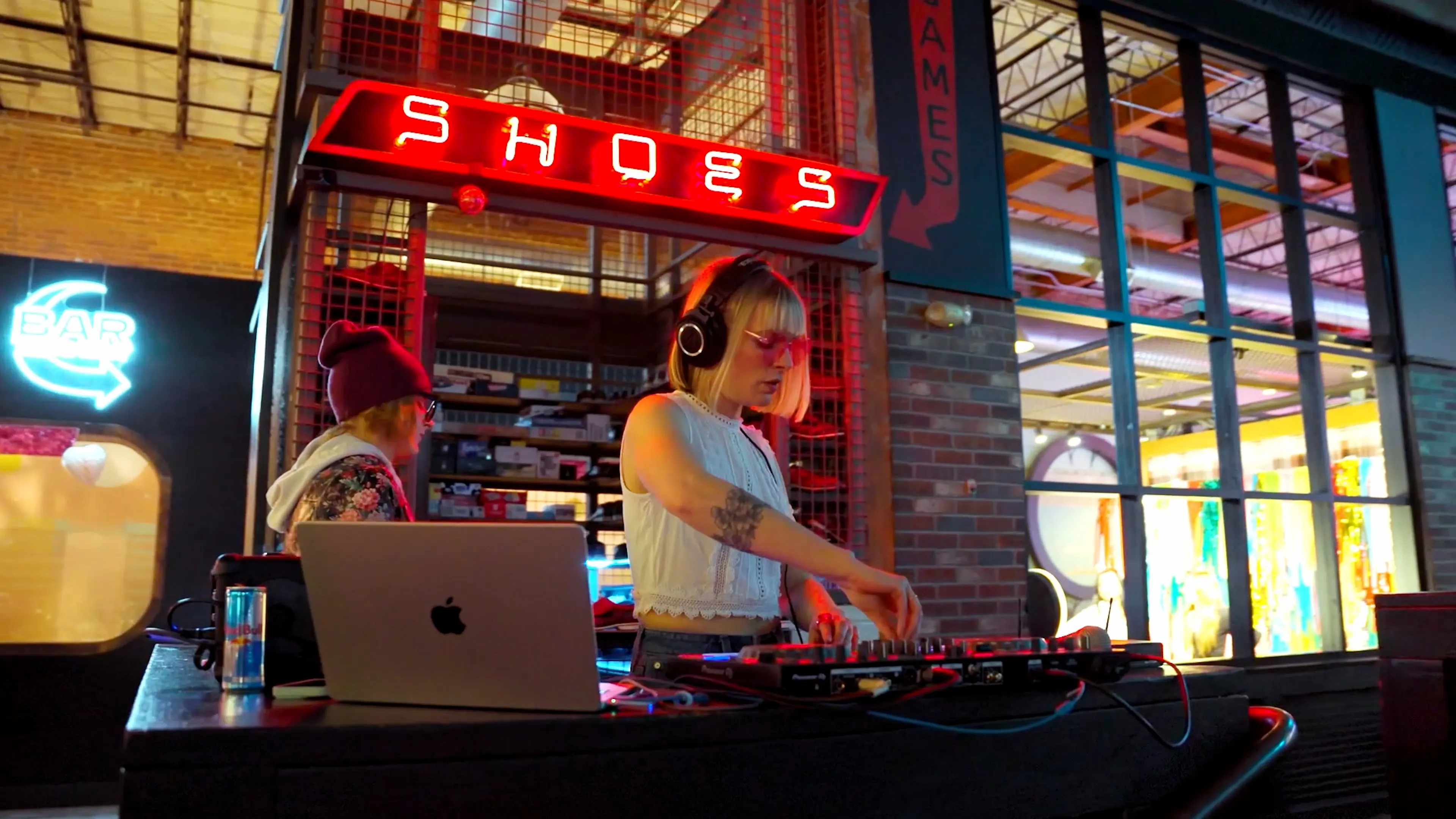 A DJ in headphones performs a live set at Punch Bowl Social beneath the venue's neon SHOES and GAMES signs